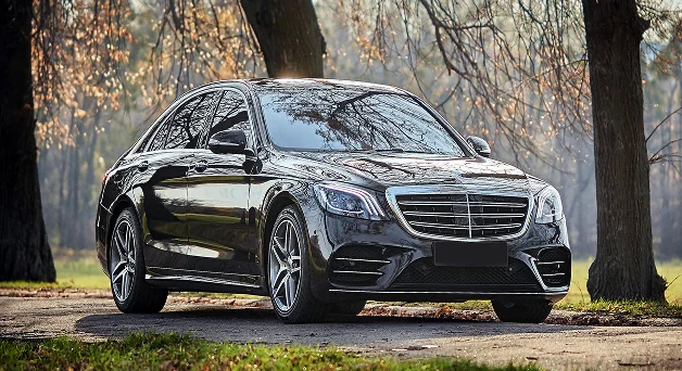 Sonbahar gün ışığında ağaçların yanında park etmiş siyah Mercedes lüks sedan.