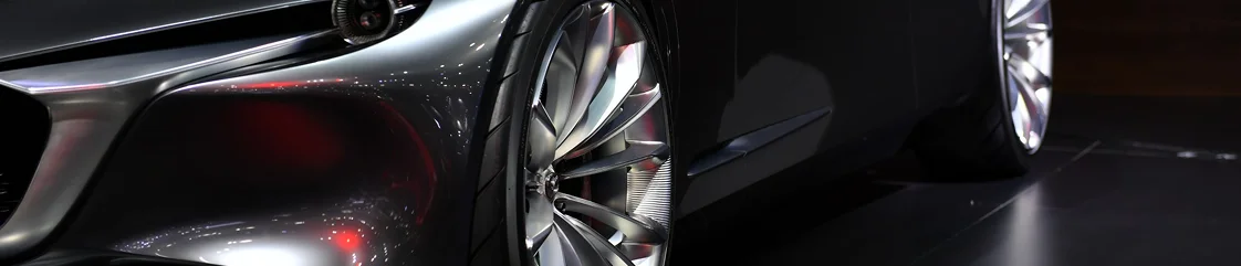 Showroom aydınlatması altında lüks spor otomobil tekerleği ve metalik gövdesinin yakın detayları.