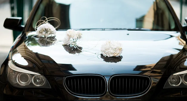 Kaputunda beyaz çiçeklerle süslenmiş siyah BMW düğün aracı.